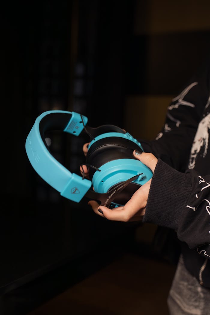 Close-up of a person holding blue headphones with a black background, showcasing modern audio gear.